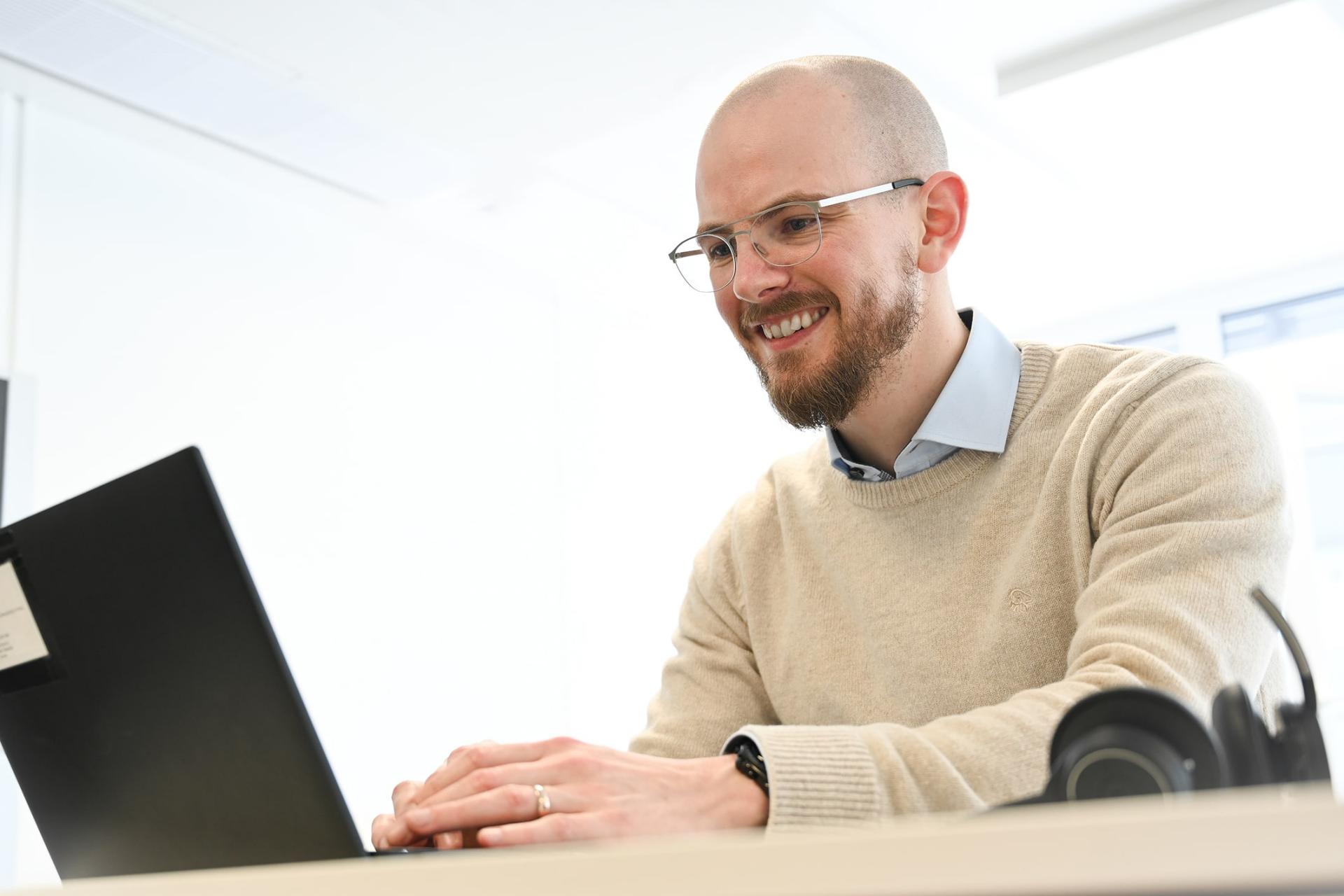 Max types on his laptop in the office, looks at the screen and smiles