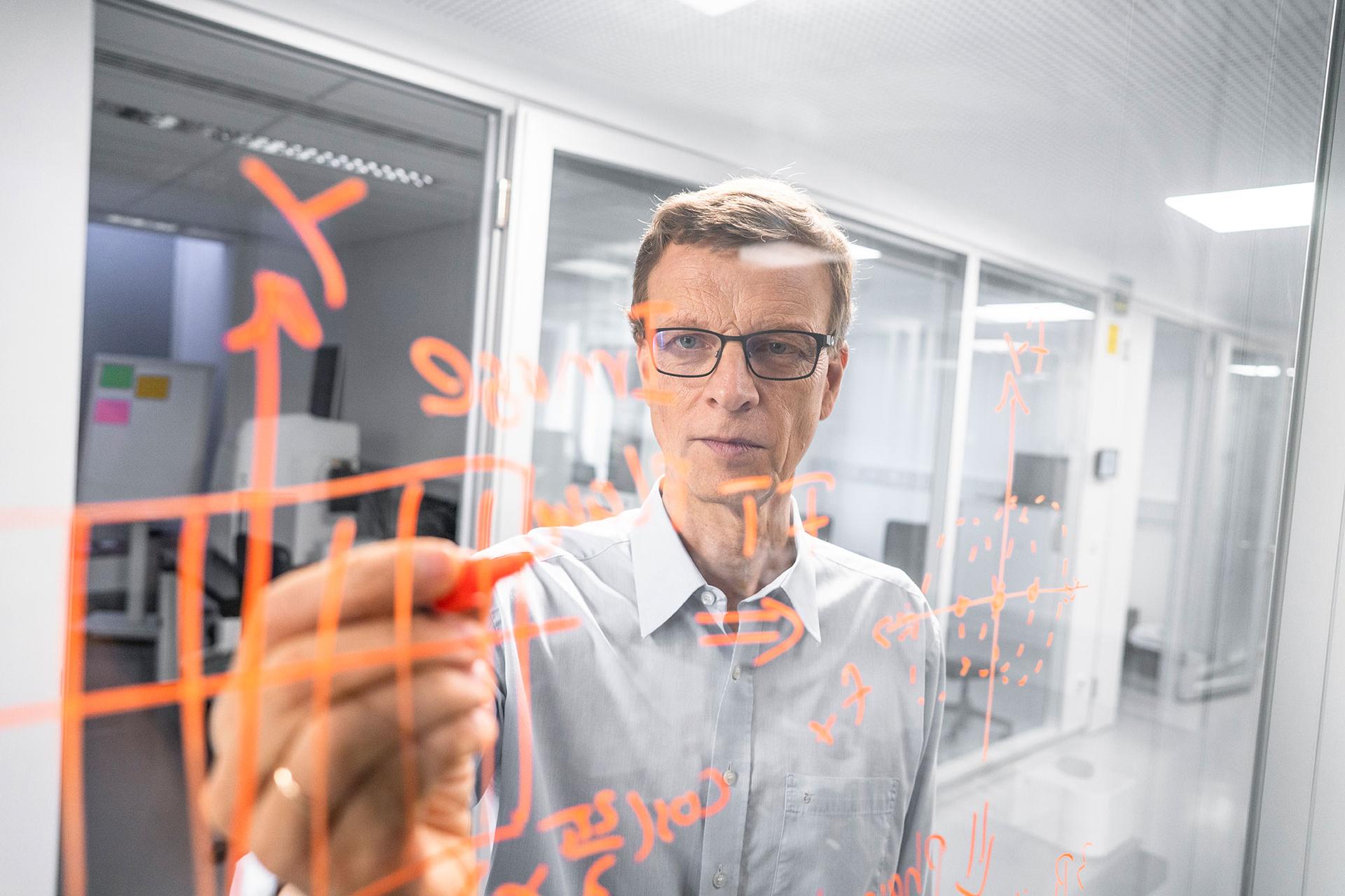 Michael draws scientific graphs and writes notes on a pane of glass in a ZEISS office.