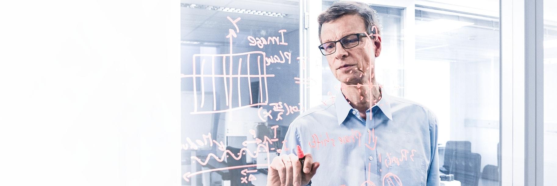 Dr. Michael Totzeck sketching scientific graphs and writing notes on a pane of glass in an office at ZEISS