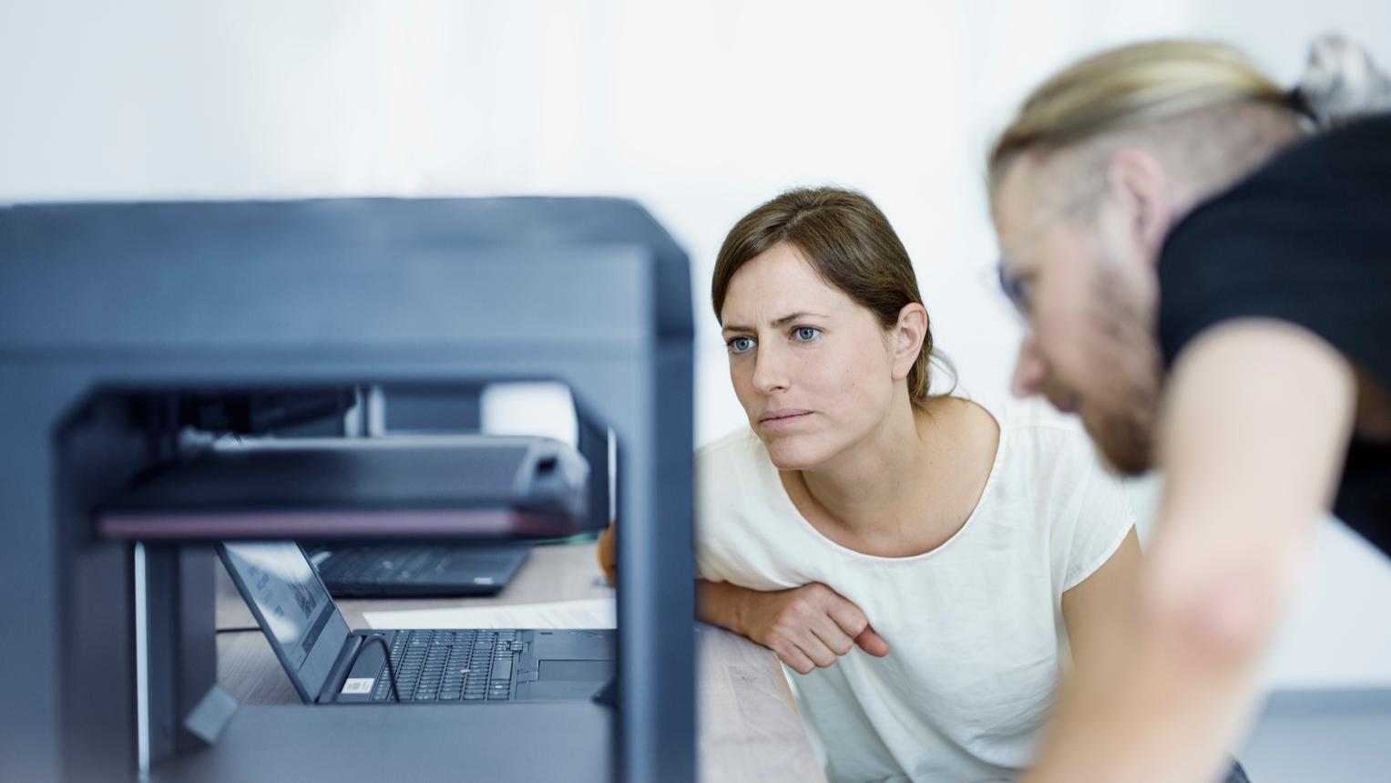 Sophia and her colleague examine a piece of equipment in the office