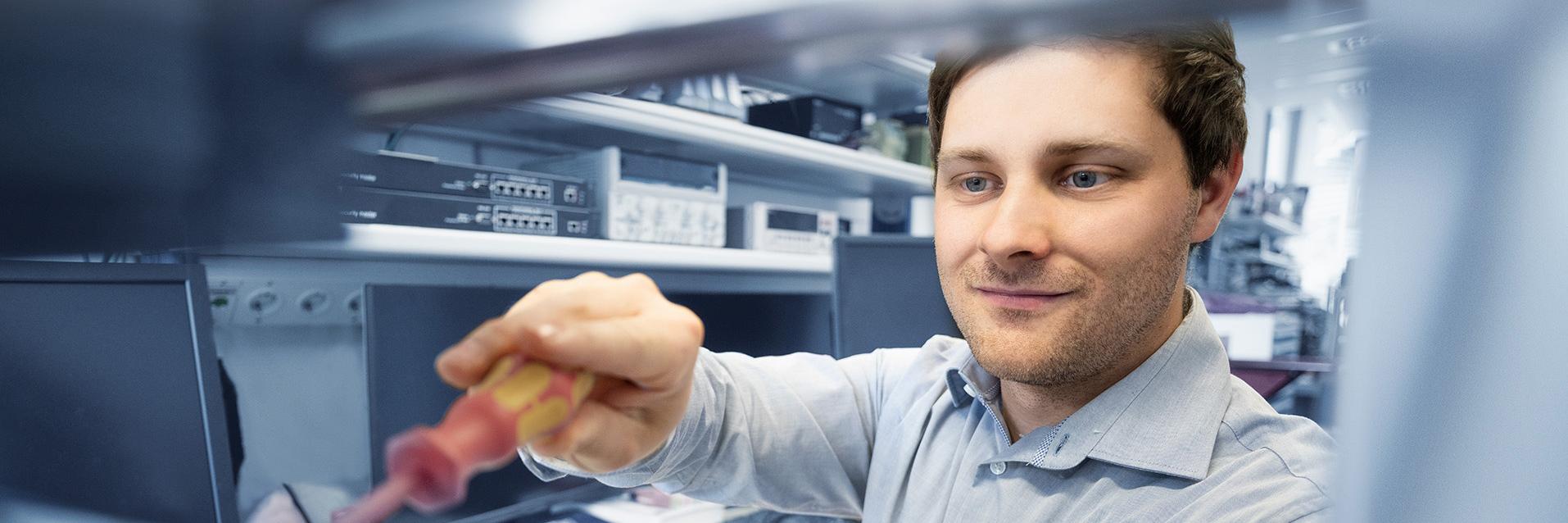 Steffen uses a screwdriver to work on an electronic device in a technical work environment.