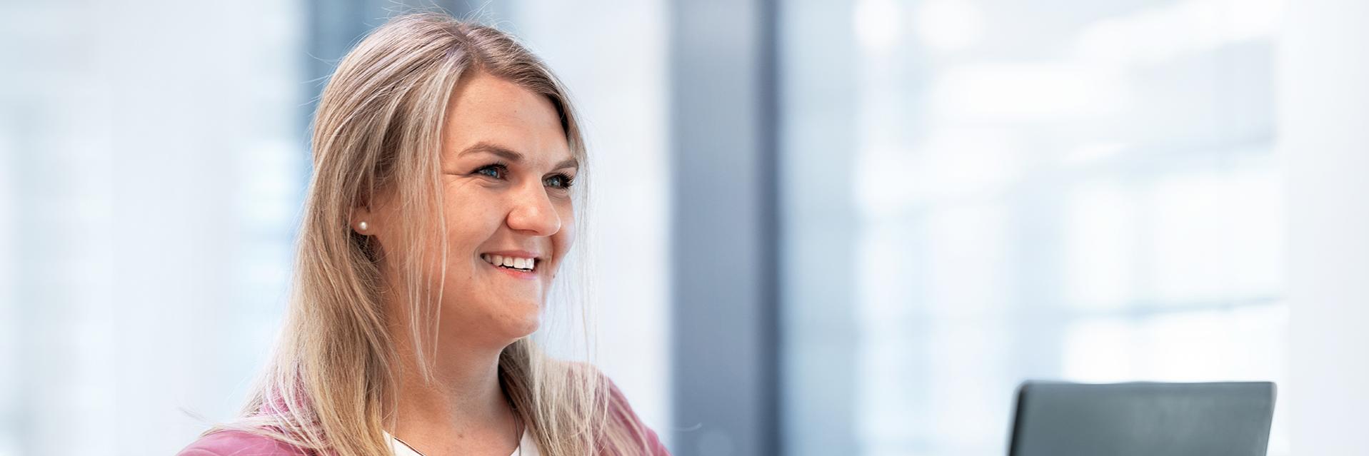 Stephanie sits in a modern ZEISS office and types on her laptop as she looks ahead with a smile.