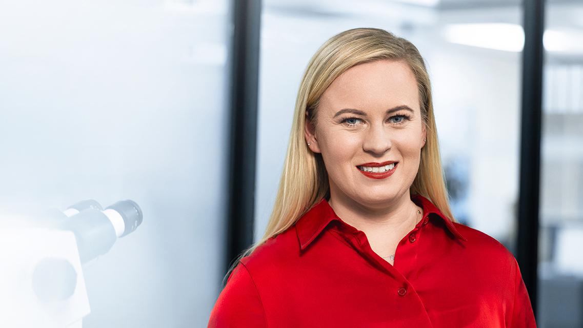 ZEISS employee women, laughing and standing beside a microscope.