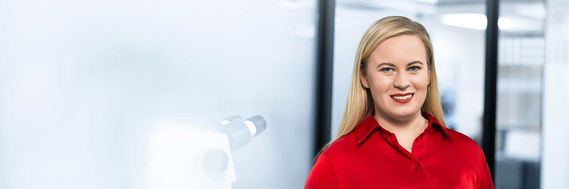 ZEISS Employee with red dress standing in her office, smiling.