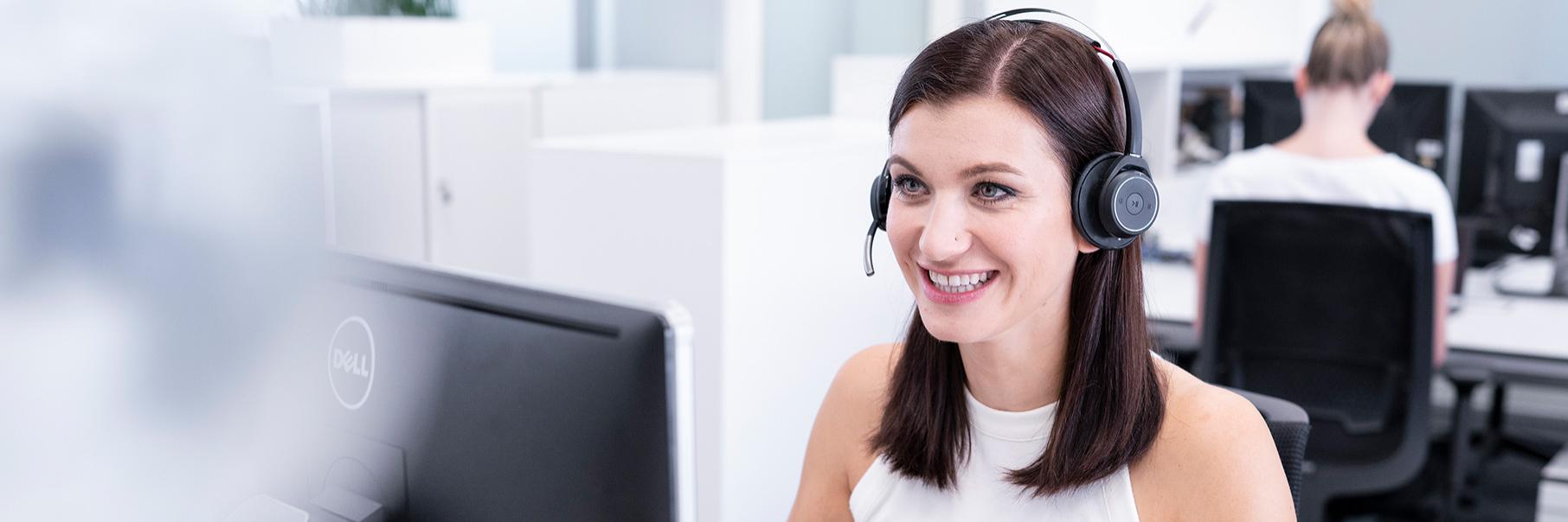 Jenny sitzt im Büro am Schreibtisch und hat ein Headset aufgesetzt