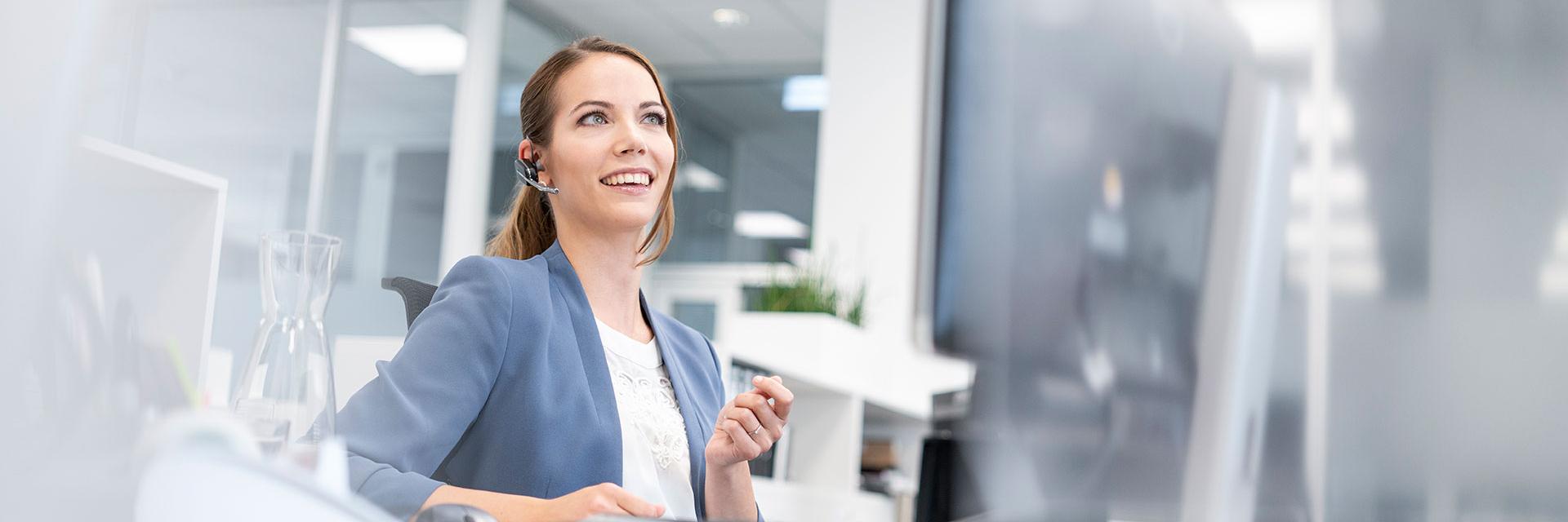 Lisa sitzt im Büro am Schreibtisch, eine Hand erhoben