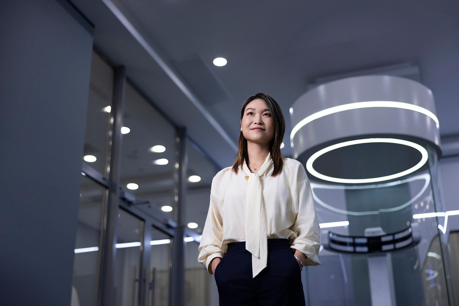 Lizzy stands proudly in front of ZEISS Vision equipment in her glass-walled office with her hands casually placed in her pockets.