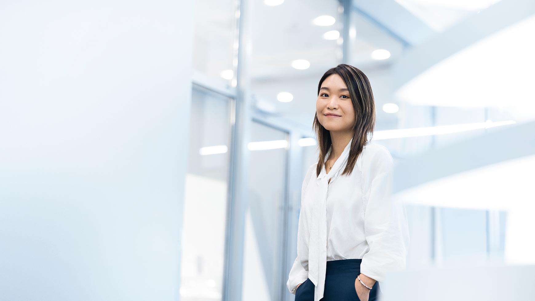 Lizzy relaxes and smiles as she stands in a bright, well-lit ZEISS building. 