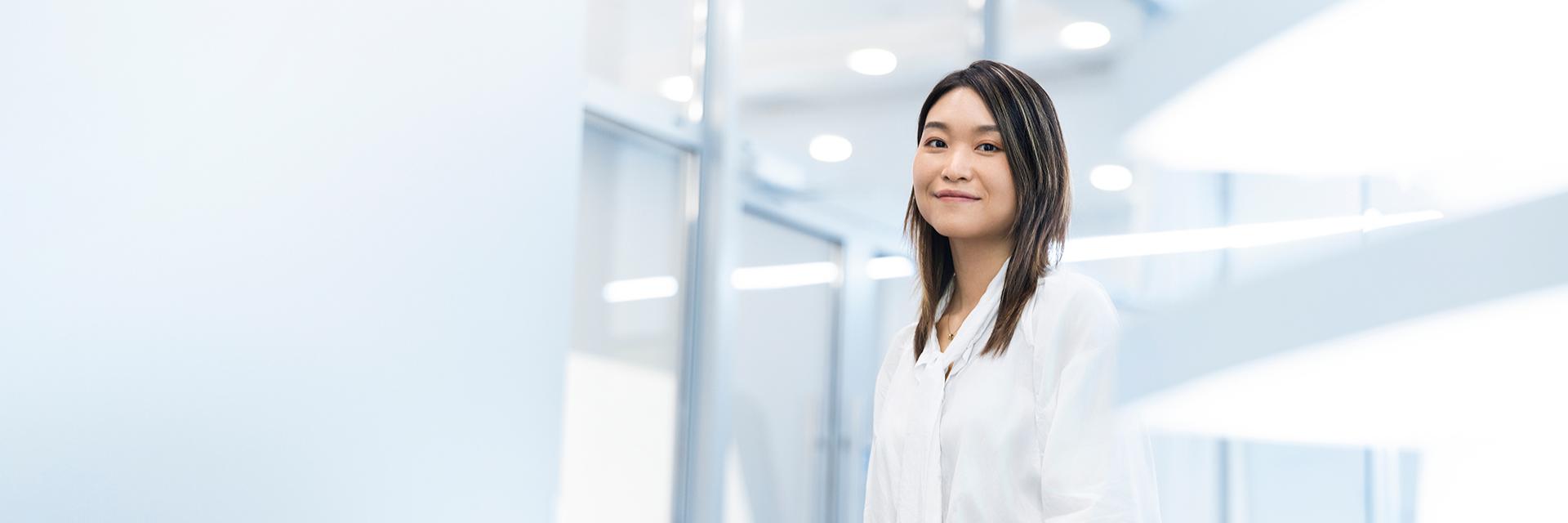Lizzy relaxes and smiles as she stands in a bright, well-lit ZEISS building. 
