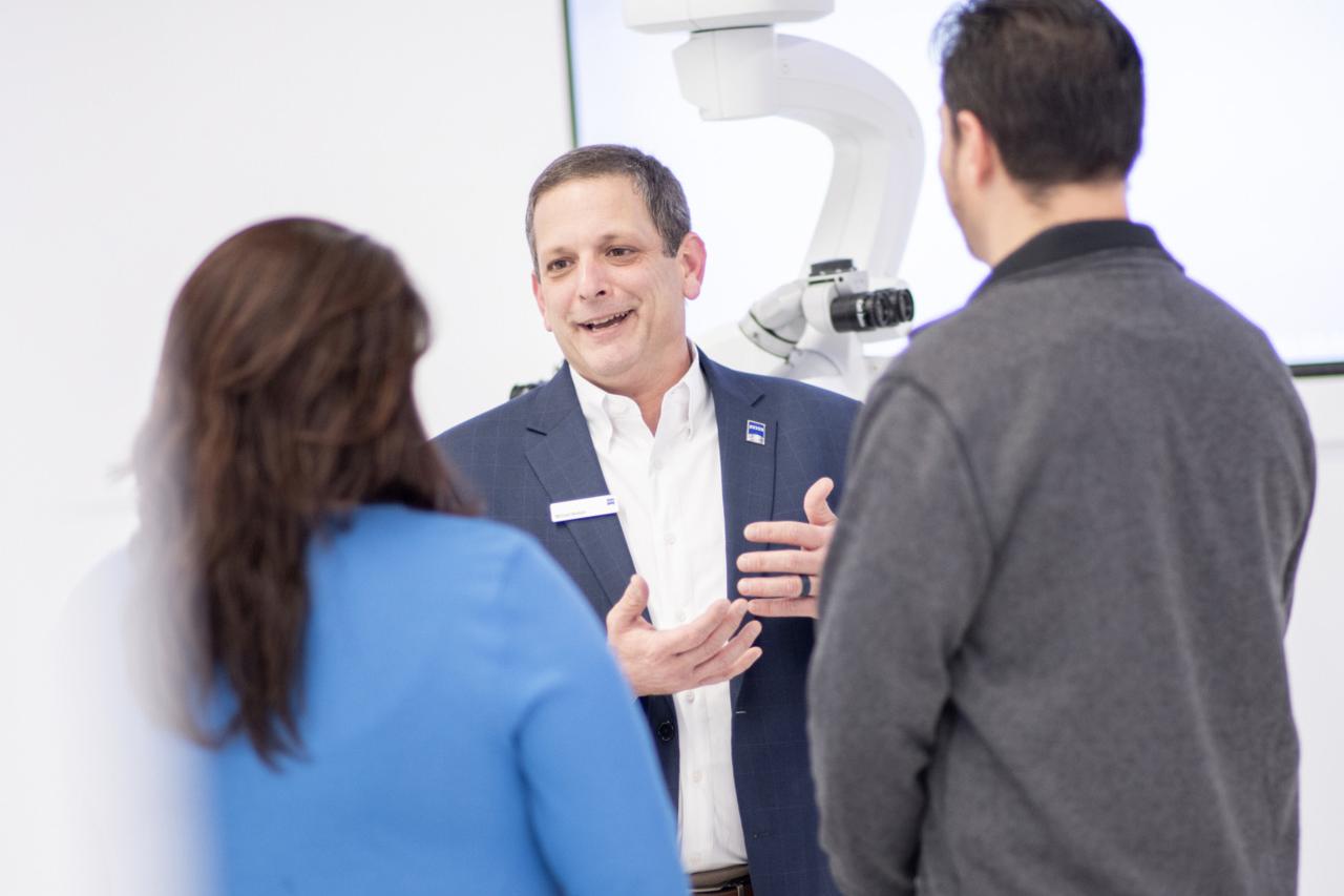 Michael führt ein Gespräch mit zwei Mitarbeitern, während er in einem gut beleuchteten Raum vor einem ZEISS Gerät steht