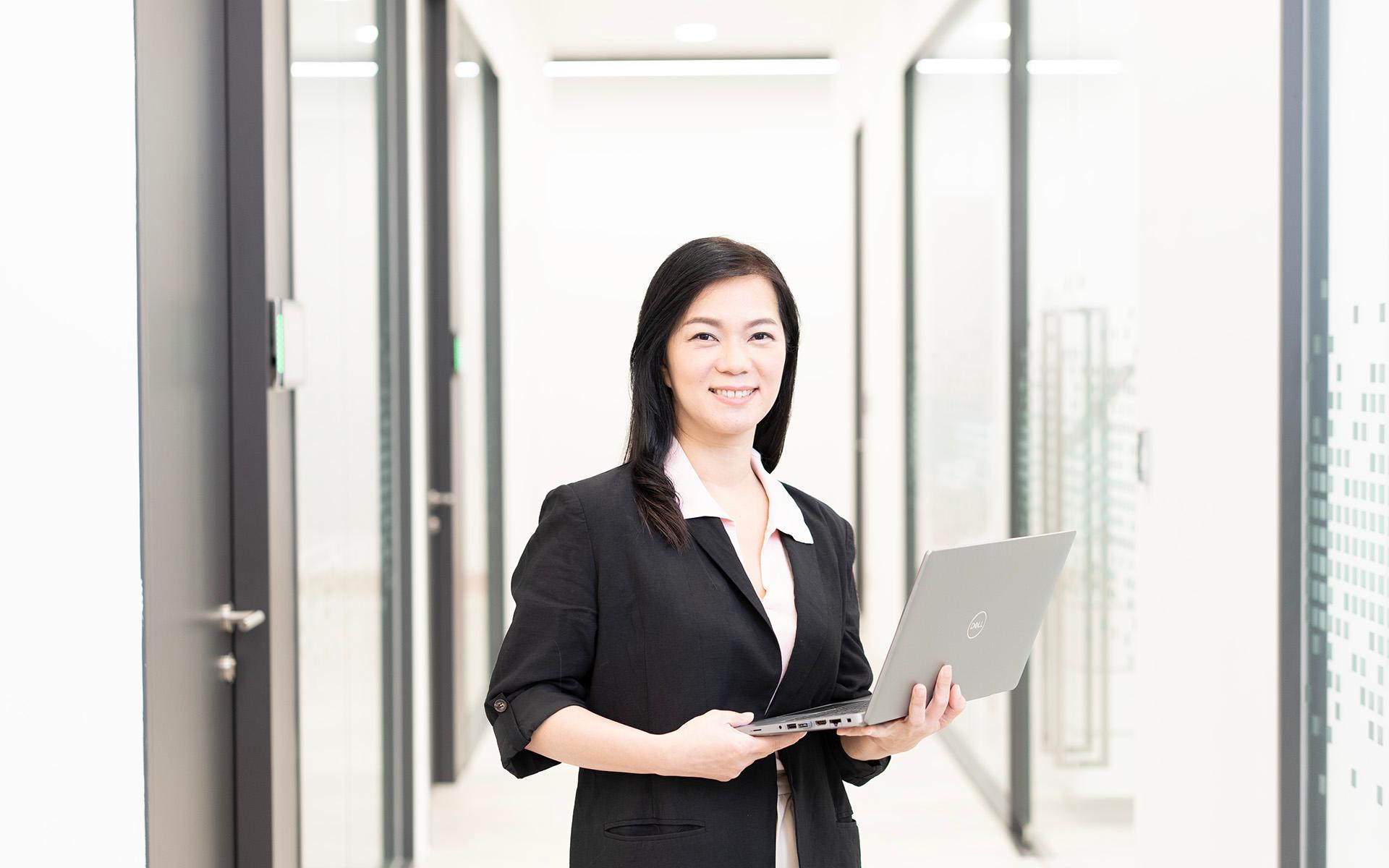ZEISS employee Vivian standing in the office hallway, holding her Laptop in her hands.