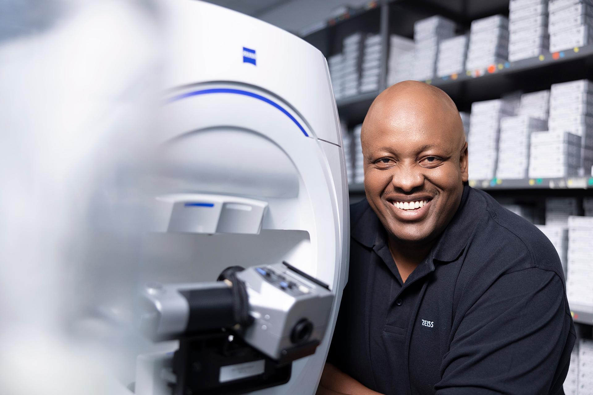 ZEISS field service Engineer Buyani is satisfied and smiles, next to a diagnostic device.