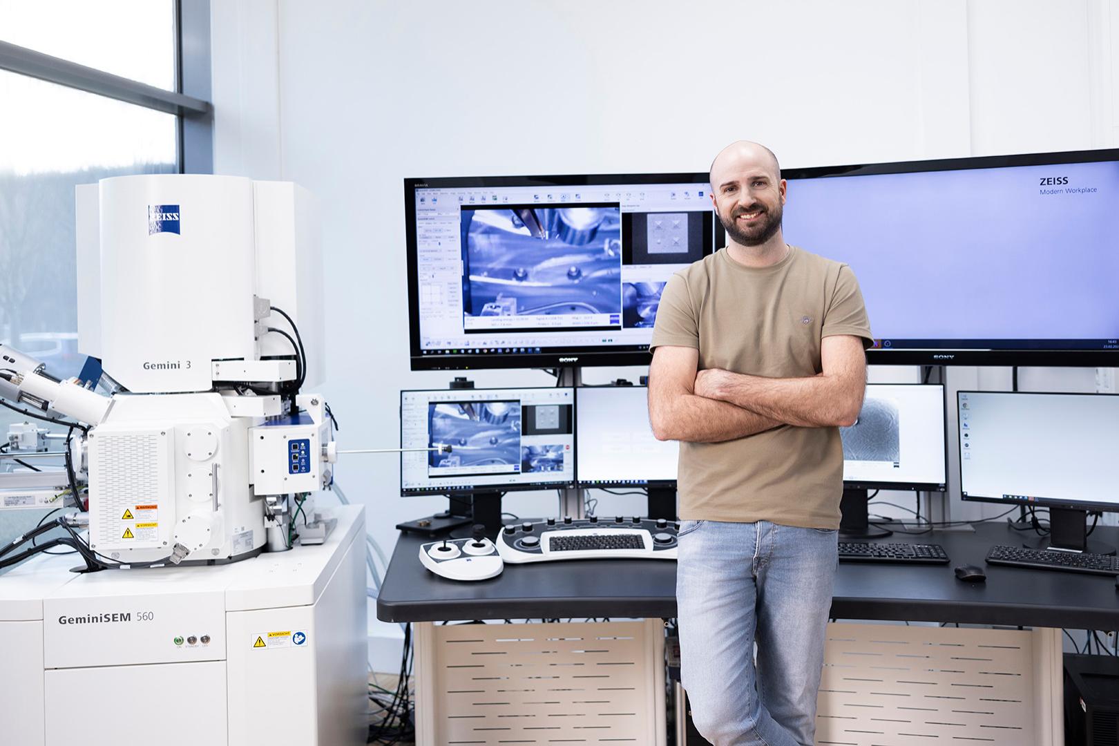 Daniel stands in a technical room with various equipment. He looks warmly at the camera