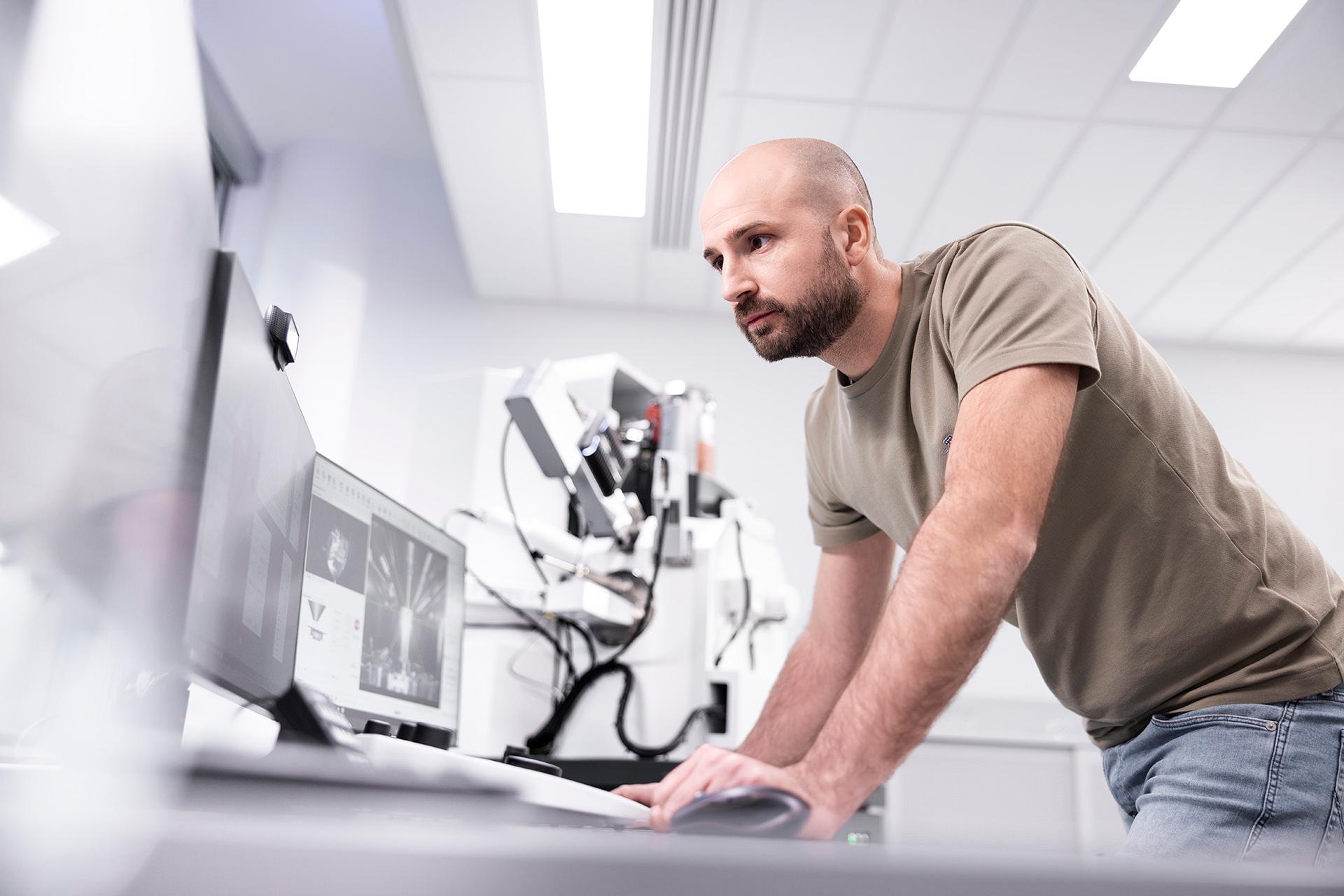 Daniel stands as he works at a desk and focuses on the monitors