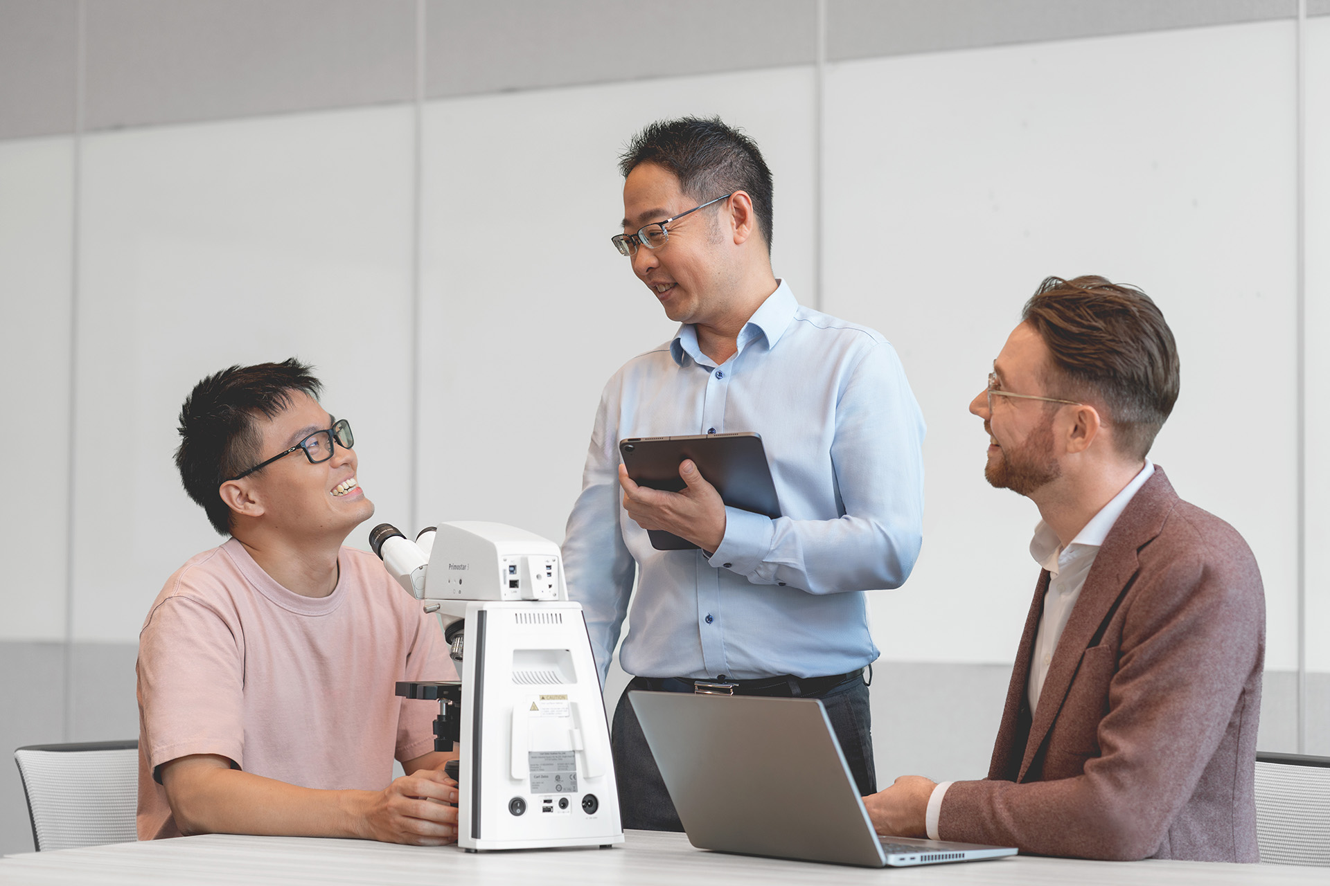 ZEISS Servicetechniker Danny spricht während der Arbeit an einem Mikroskop mit zwei Kollegen