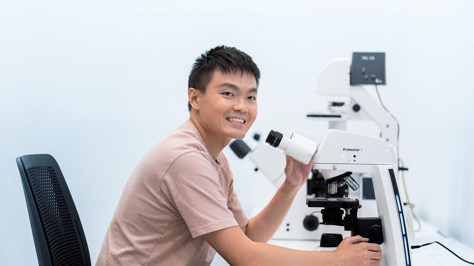 ZEISS field service engineer Danny sits at a microscope and smiles.