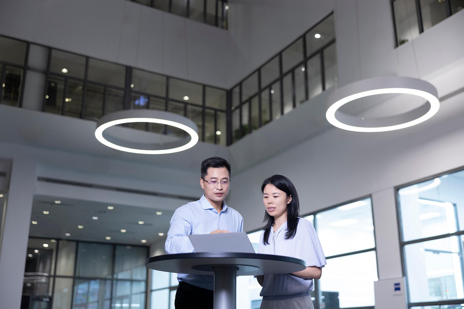 Jun and a female ZEISS colleague are discussing something at a laptop in a spacious lobby