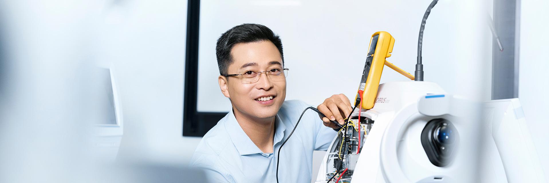 ZEISS employee Jun is using a digital multimeter to work on a medical device from the ZEISS Cirrus series.