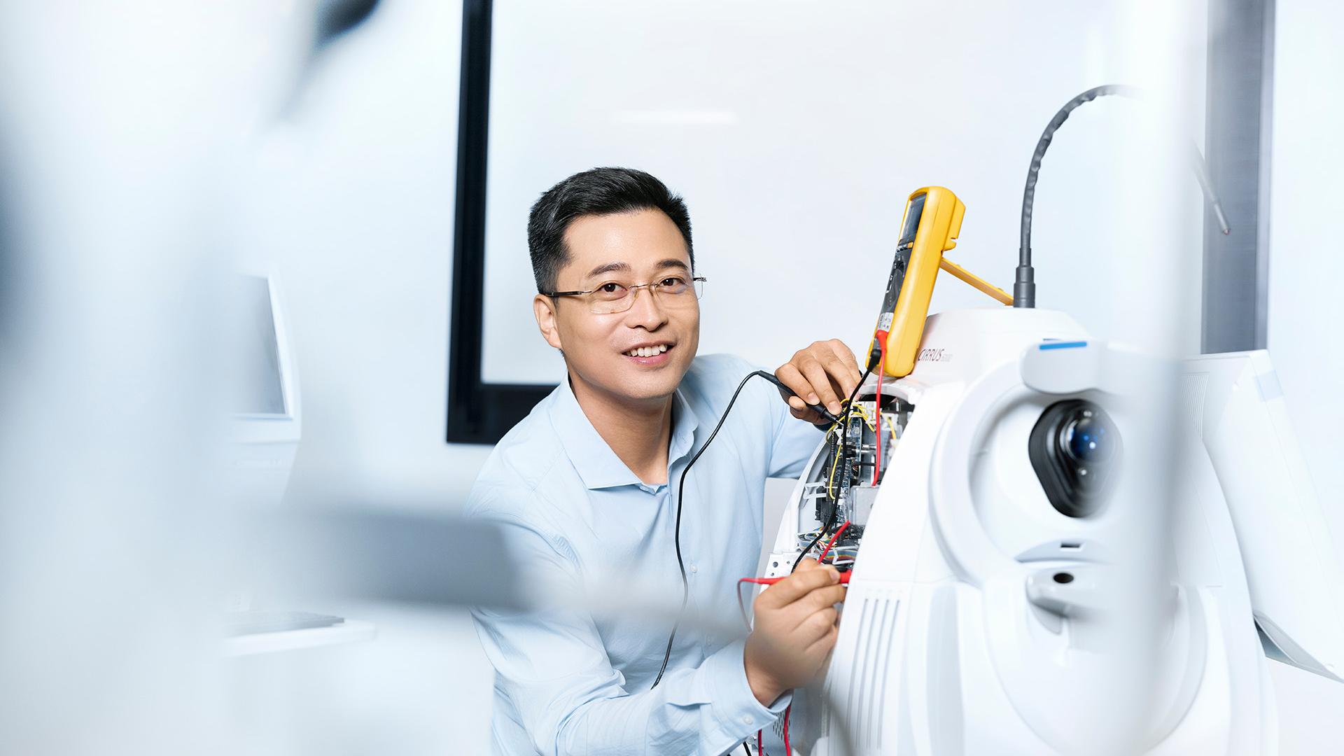 ZEISS employee Jun is using a digital multimeter to work on a medical device from the ZEISS Cirrus series.