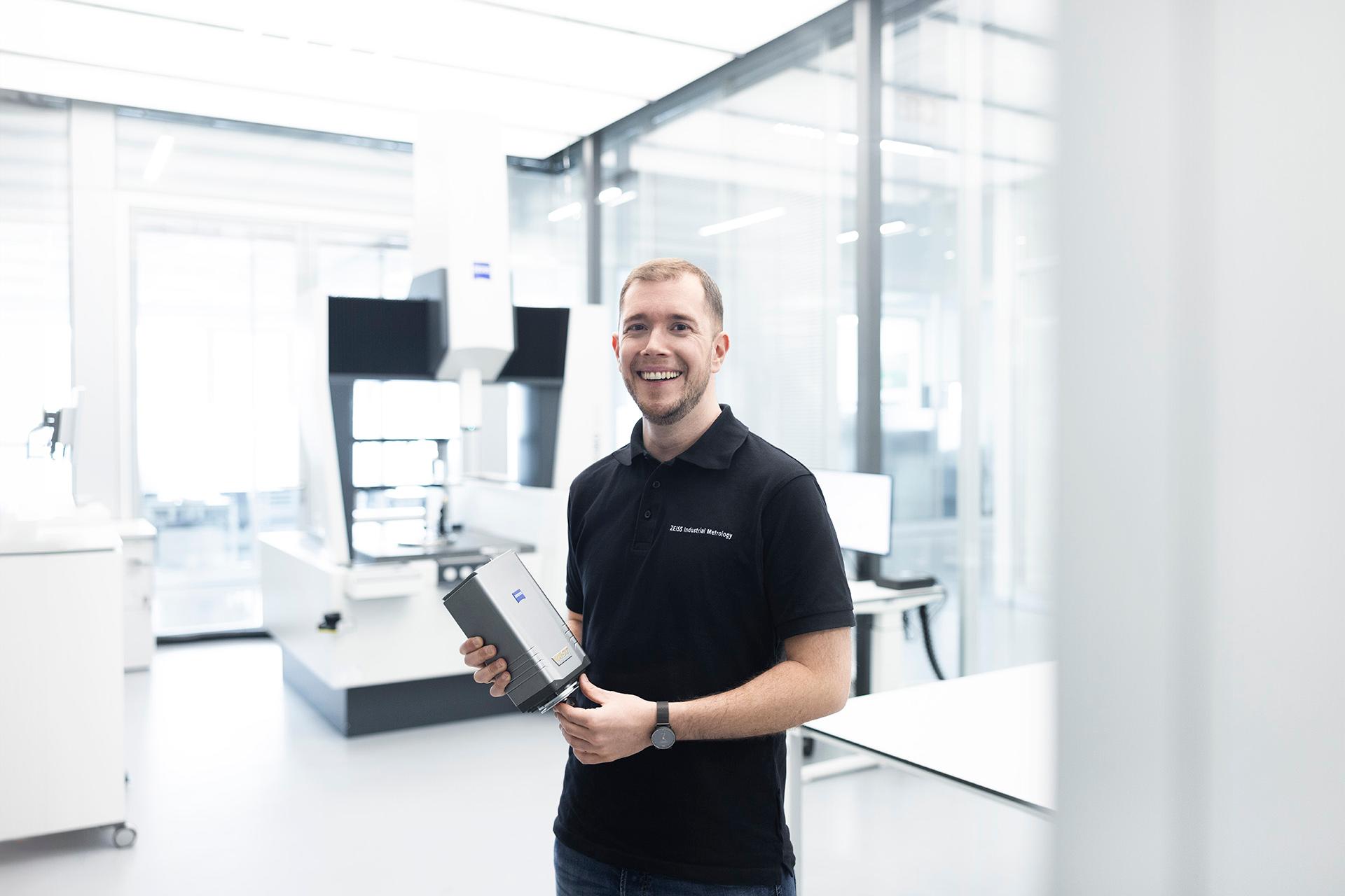 Marwin stands in a ZEISS manufacturing room and smiles as he looks directly at the camera