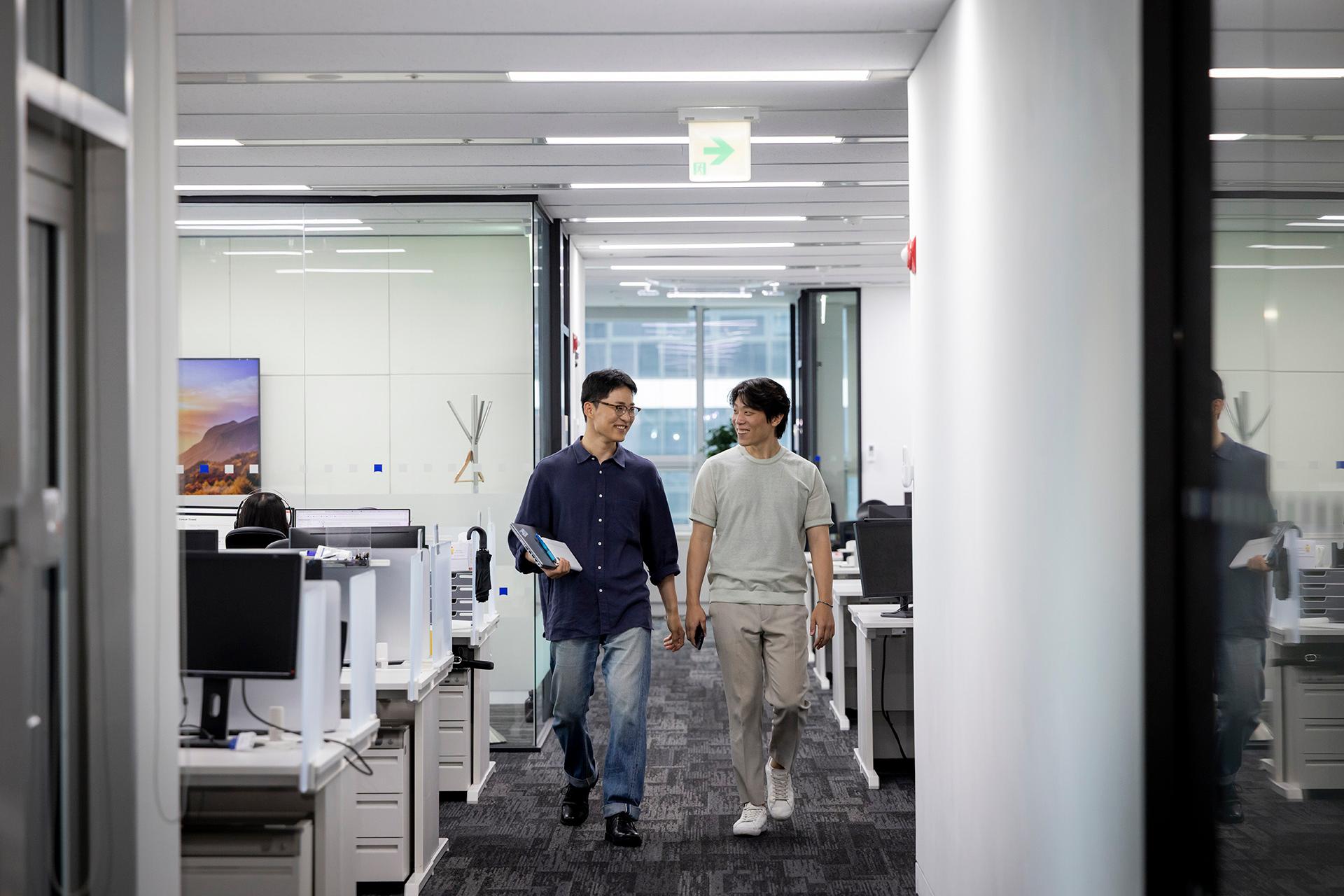 ZEISS employee MinKyue walking with his colleague through the office, laughing together.