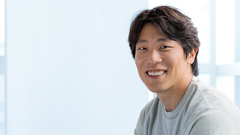 ZEISS-Mitarbeitender MinKyue sitzt lachend in seinem Büro.