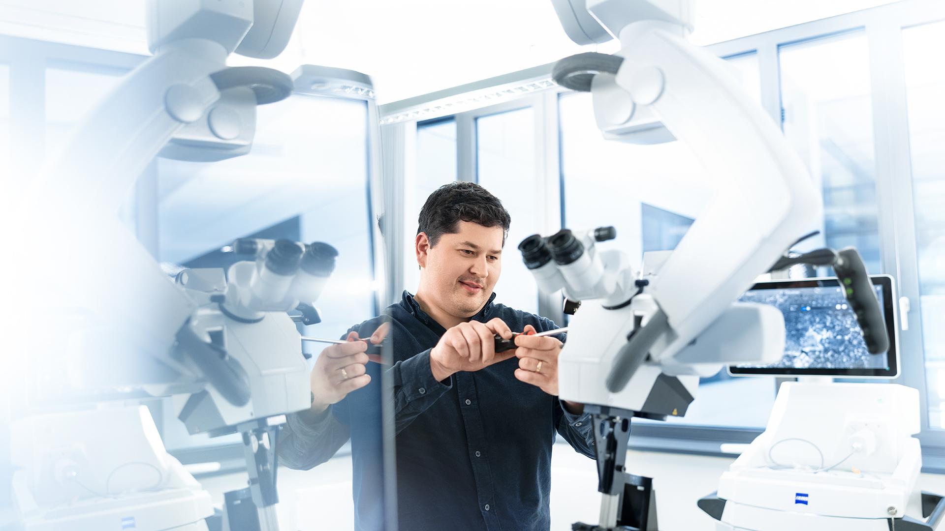 ZEISS Servicetechniker Patrick arbeitet konzentriert, aber lächelnd an einem Mikroskop und schraubt an einem technischen Detail.