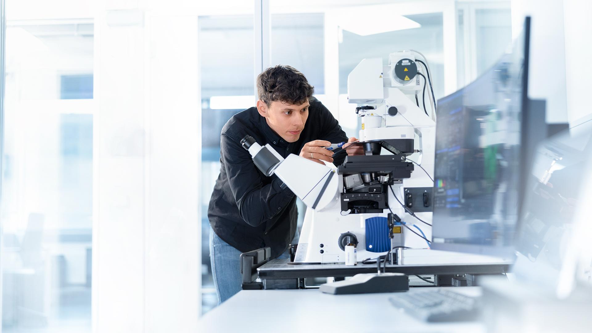 ZEISS Servicetechniker Robin steht an einem Mikroskop und schraubt konzentriert an der Verkleidung des Gerätes.