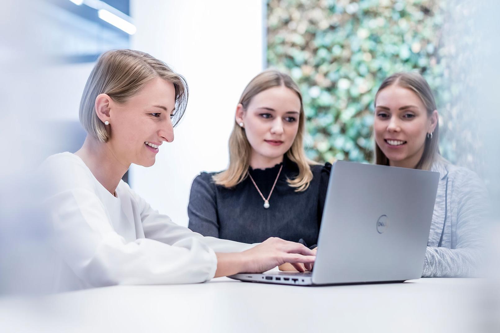 Anna works on a laptop with two colleagues