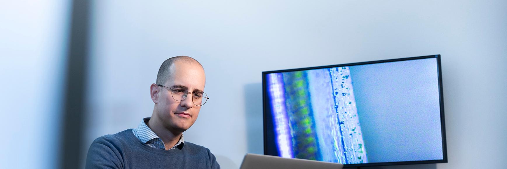 Sam sitzt konzentriert am Schreibtisch und arbeitet am Computer in einem separtem ZEISS Büro.