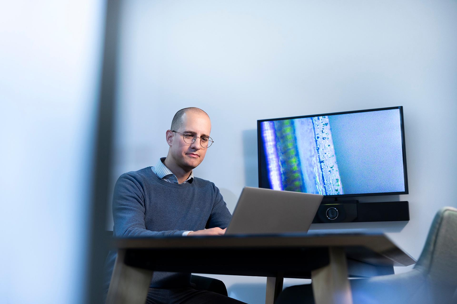Sam sitzt konzentriert am Schreibtisch und arbeitet am Computer in einem separtem ZEISS Büro.