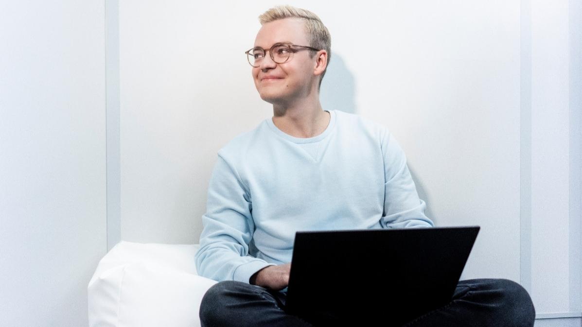 Ein junger Mann sitzt entspannt auf einem Sitzkissen, während er an seinem Laptop arbeitet