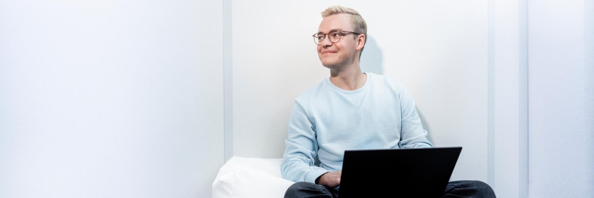 Ein junger Mann sitzt entspannt auf einem Sitzkissen, während er auf seinem Laptop arbeitet