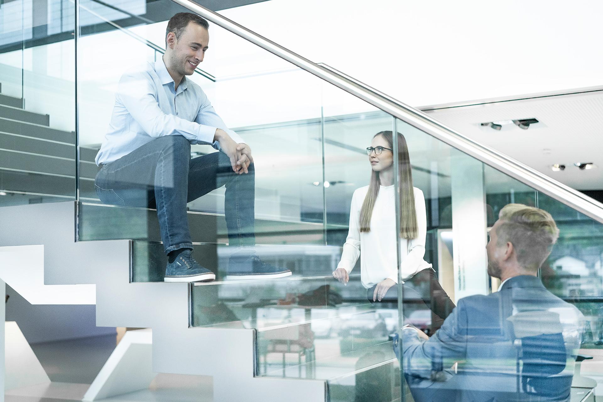 Three young people sit on a staircase with glass balustrades