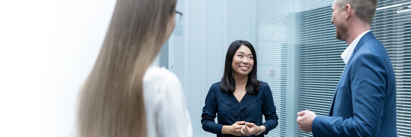 Three people stand and talk in a modern office environment