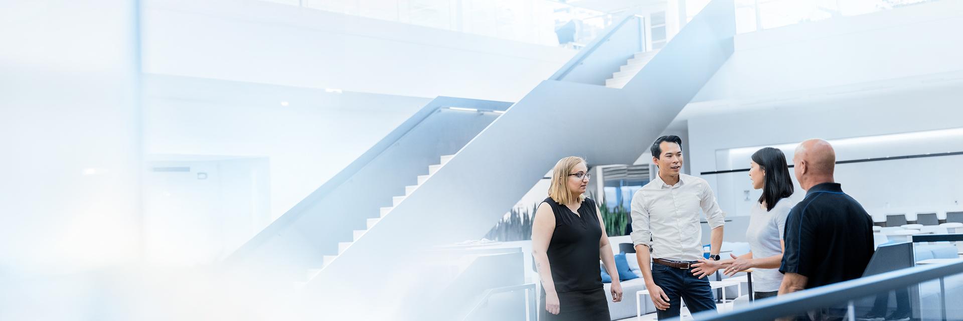 Vier Personen stehen in einem modernen Bürogebäude zusammen und unterhalten sich