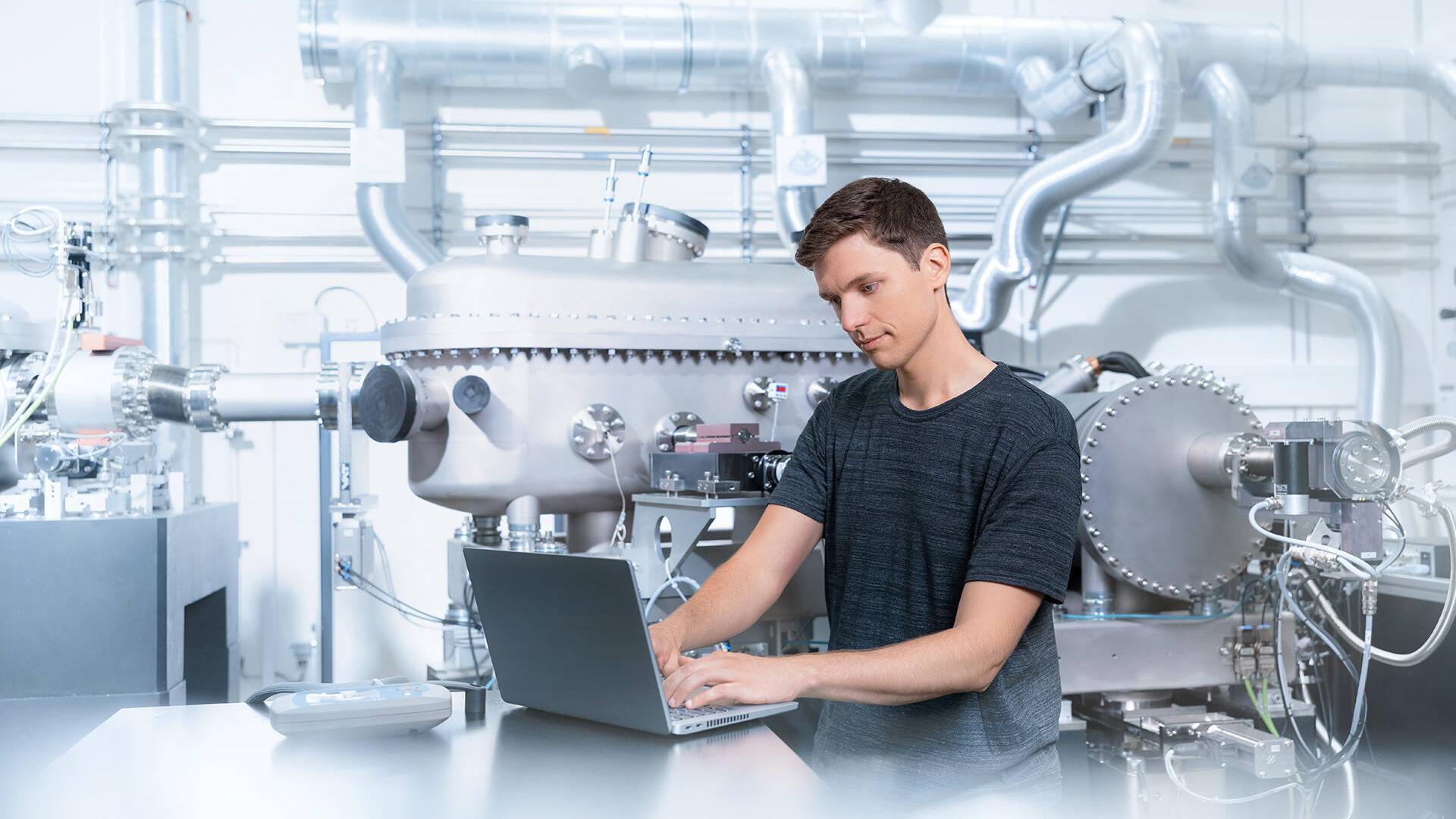 Bernhard steht in einem Produktionsraum und schaut auf einen Laptop