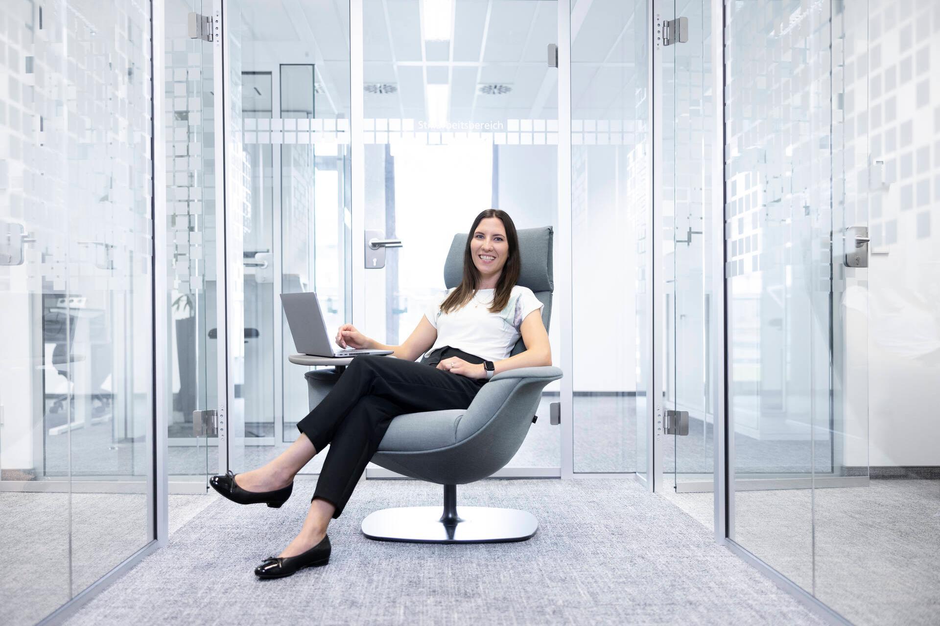 Marina sitzt in einem modernen, gläsernen Büro im Sessel und schaut in die Kamera