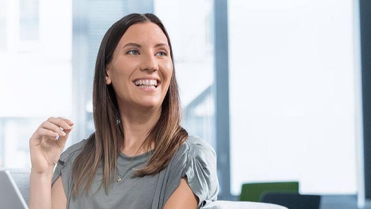 Marina sitzt in einem modernen, gläsernen Büro im Sessel und schaut in die Kamera