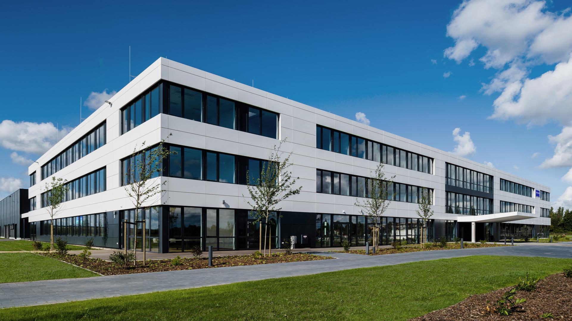 The office building of Carl Zeiss GOM Metrology with glass windows, surrounded by green spaces and a clear blue sky.