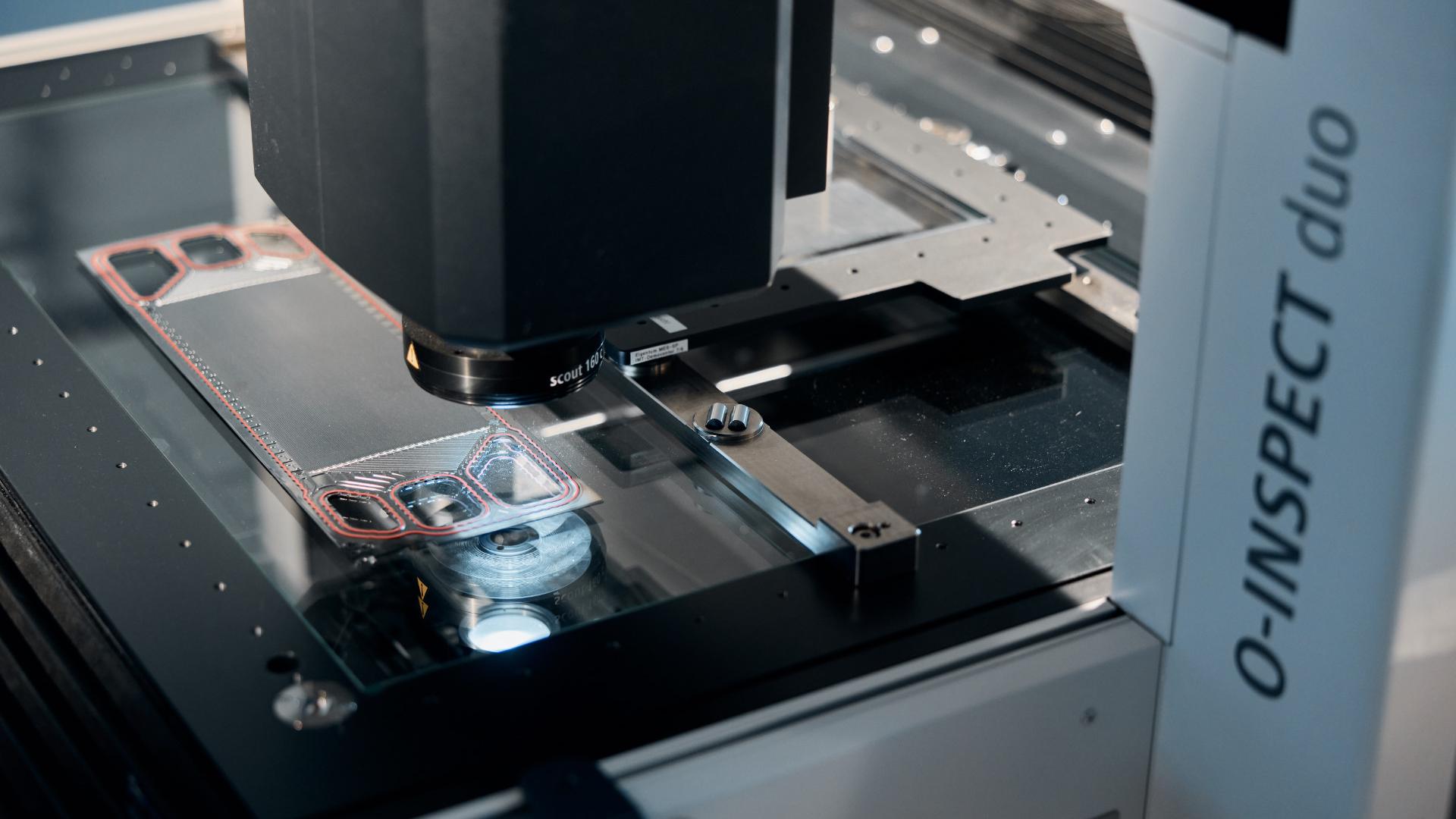 Close-up of a ZEISS O-INSPECT duo machine inspecting a metal component on its measurement platform.