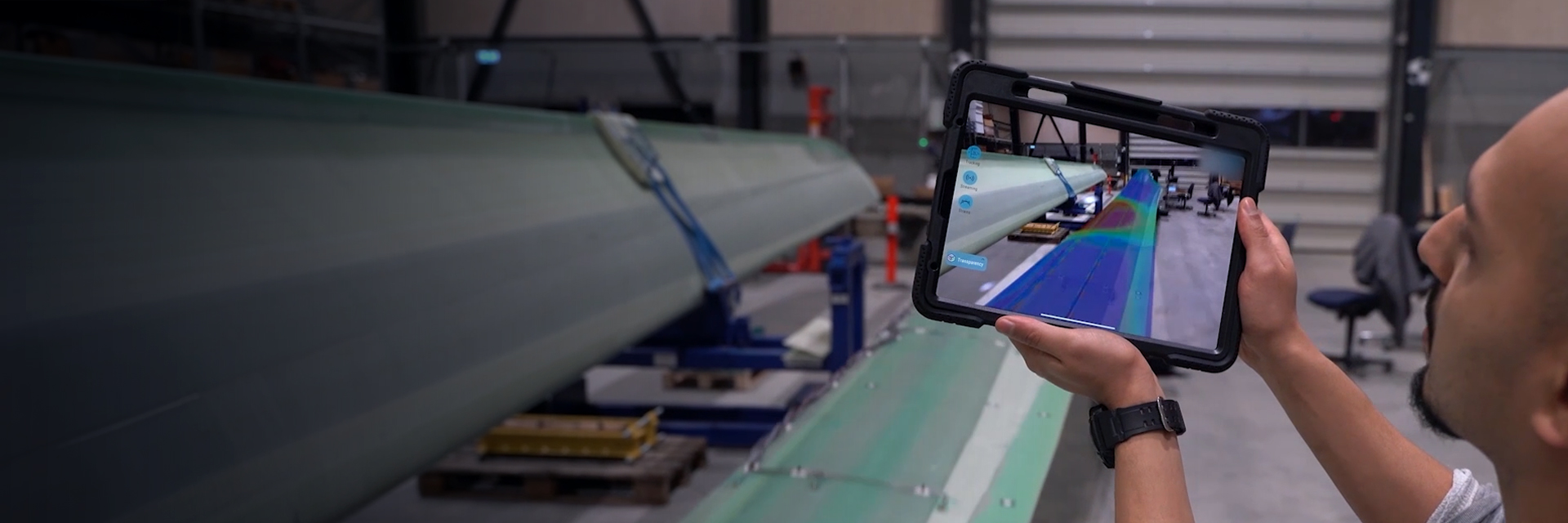 A man showing a tablet infront of an industrial part.