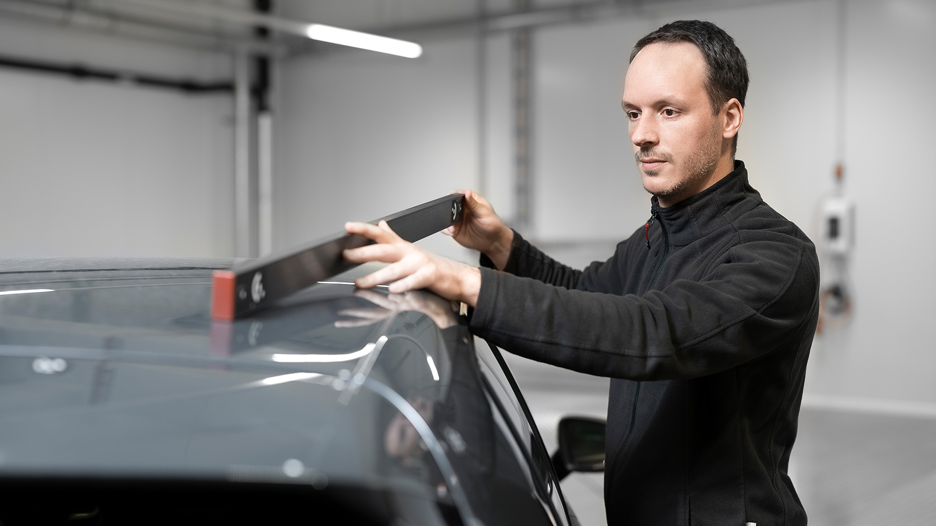 A man uses a length scale as a reference to measure the body of a car.