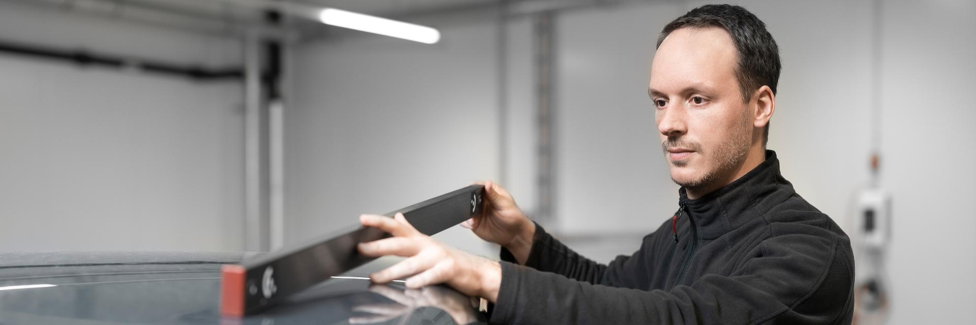 A man uses a length scale as a reference to measure the body of a car.