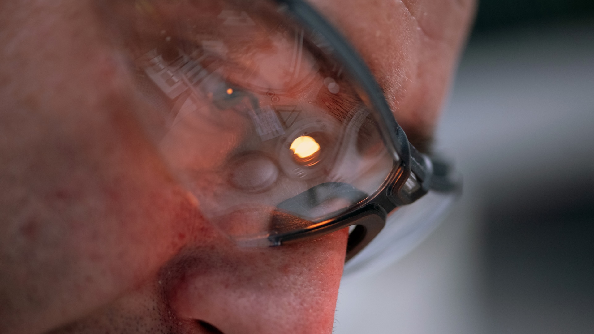 Close-up of a person wearing glasses with the reflection of a ZEISS optical device and a glowing light visible in the lenses.