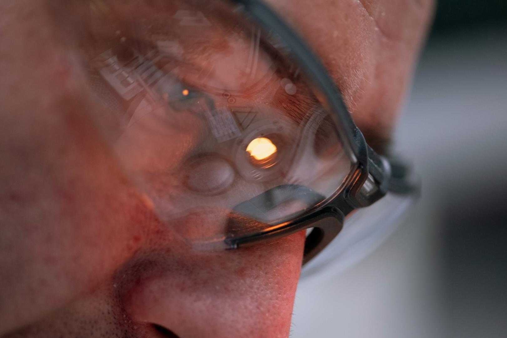 Close-up of a person wearing glasses with the reflection of a ZEISS optical device and a glowing light visible in the lenses.
