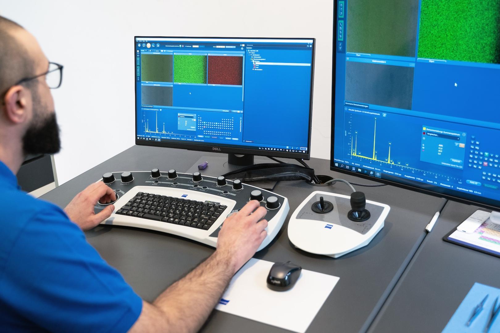 A technician operates ZEISS imaging software on dual monitors using a specialized control console in a laboratory setting.