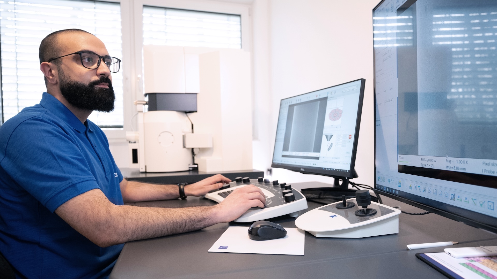 A technician operates a ZEISS instrument and analyzes data on dual monitors in a modern laboratory setting.