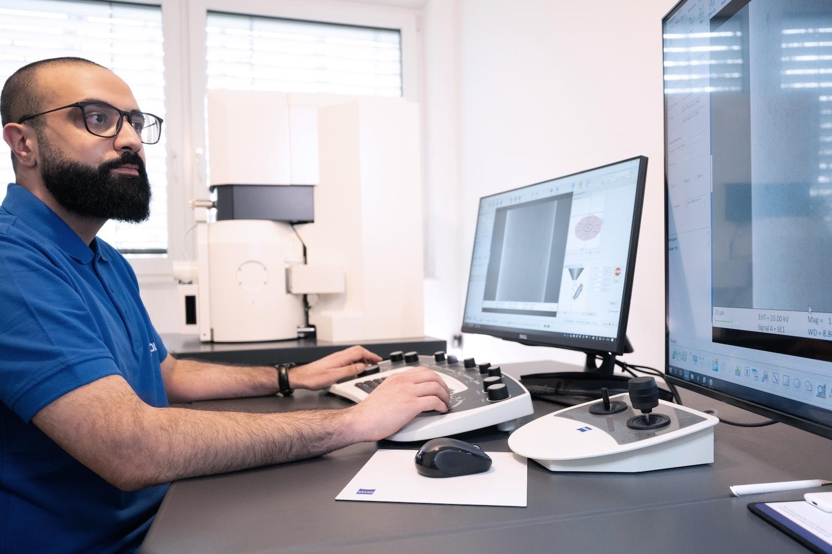 A technician operates a ZEISS instrument and analyzes data on dual monitors in a modern laboratory setting.