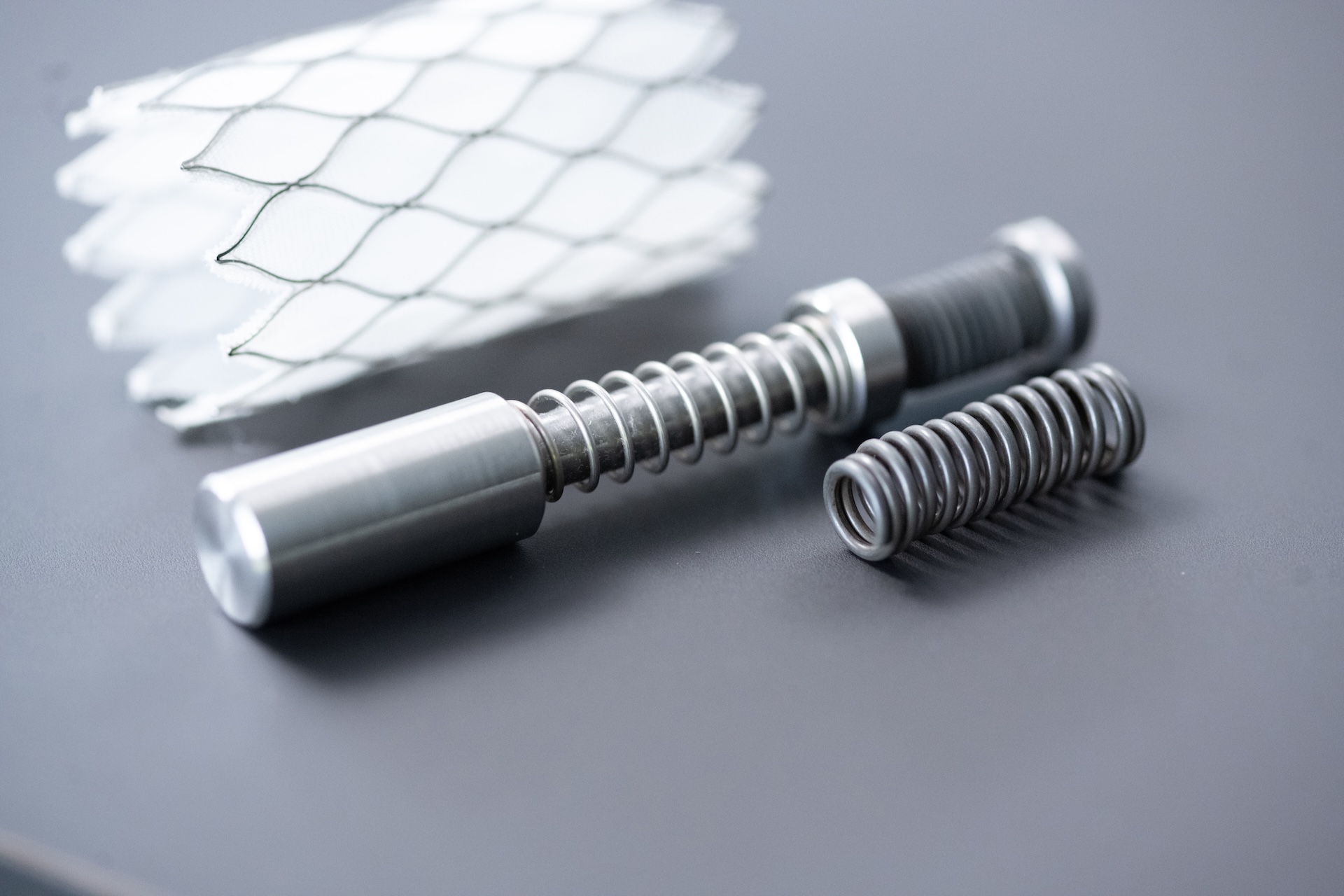 Close-up of precision-engineered metal springs and components alongside a white mesh structure on a grey surface, representing ZEISS industrial technology.